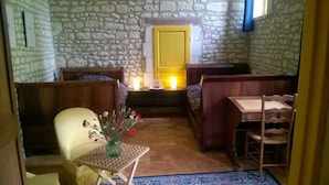 Une pièce chaleureuse avec un mur en pierre, un banc en bois, une petite table ornée d’un vase de fleurs et un lit avec une tête de lit jaune.