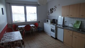 A compact kitchen with a dining area, featuring a window, a microwave, a stove, and a sink. - Zimmervermietung Lösken 1 (Duisburg)