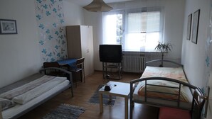 A small, sparsely furnished room with a bed, a desk, a television, and a radiator. - Zimmervermietung Lösken 1 (Duisburg)