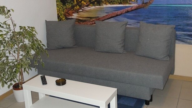 A living room with a grey sofa, a white coffee table, and a tropical beach mural on the wall.