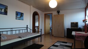 A room with a bed, a TV, a wardrobe, and a door leading to another room.