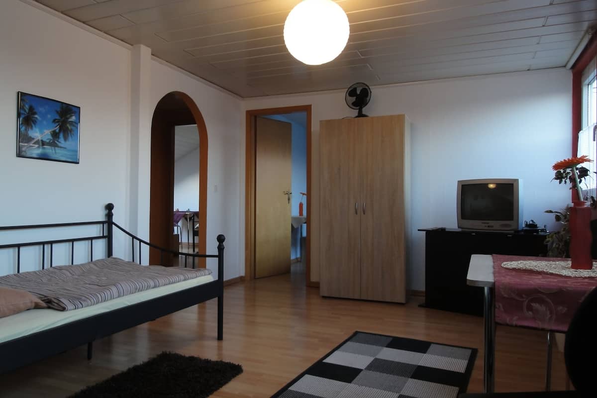 Ein Zimmer mit einem Bett, einem Fernseher, einem Kleiderschrank und einer Tür zu einem anderen Raum.
