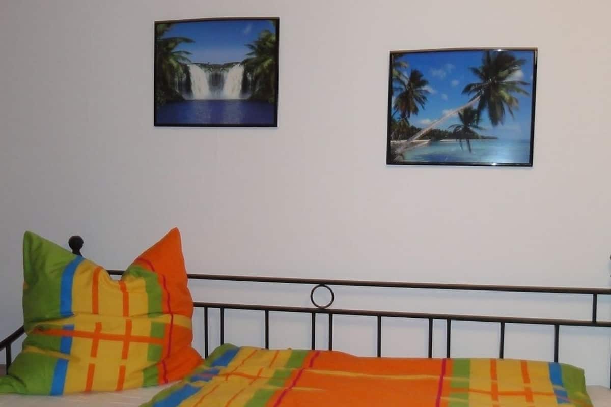 Ein Zimmer mit einem Bett, zwei Bildern an der Wand und einem Holzboden.