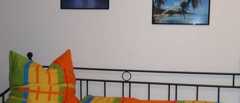 A room with a bed, two wall-mounted pictures, and a wooden floor.