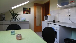 A compact kitchen with a microwave, a small refrigerator, and a sink. There's a dining table with chairs and a potted plant.