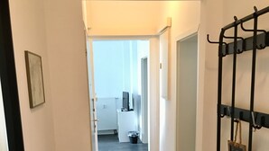 Um corredor com piso de madeira, um banco preto, um cabideiro e uma porta que dá para uma área de cozinha.