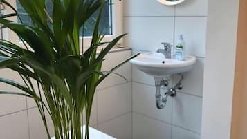 Ein Badezimmer mit einer Topfpflanze, einem Waschbecken und einem Spiegel mit Beleuchtung.