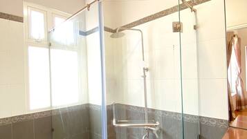 Zona de ducha con puerta de cristal, paredes de azulejos y techo de madera.