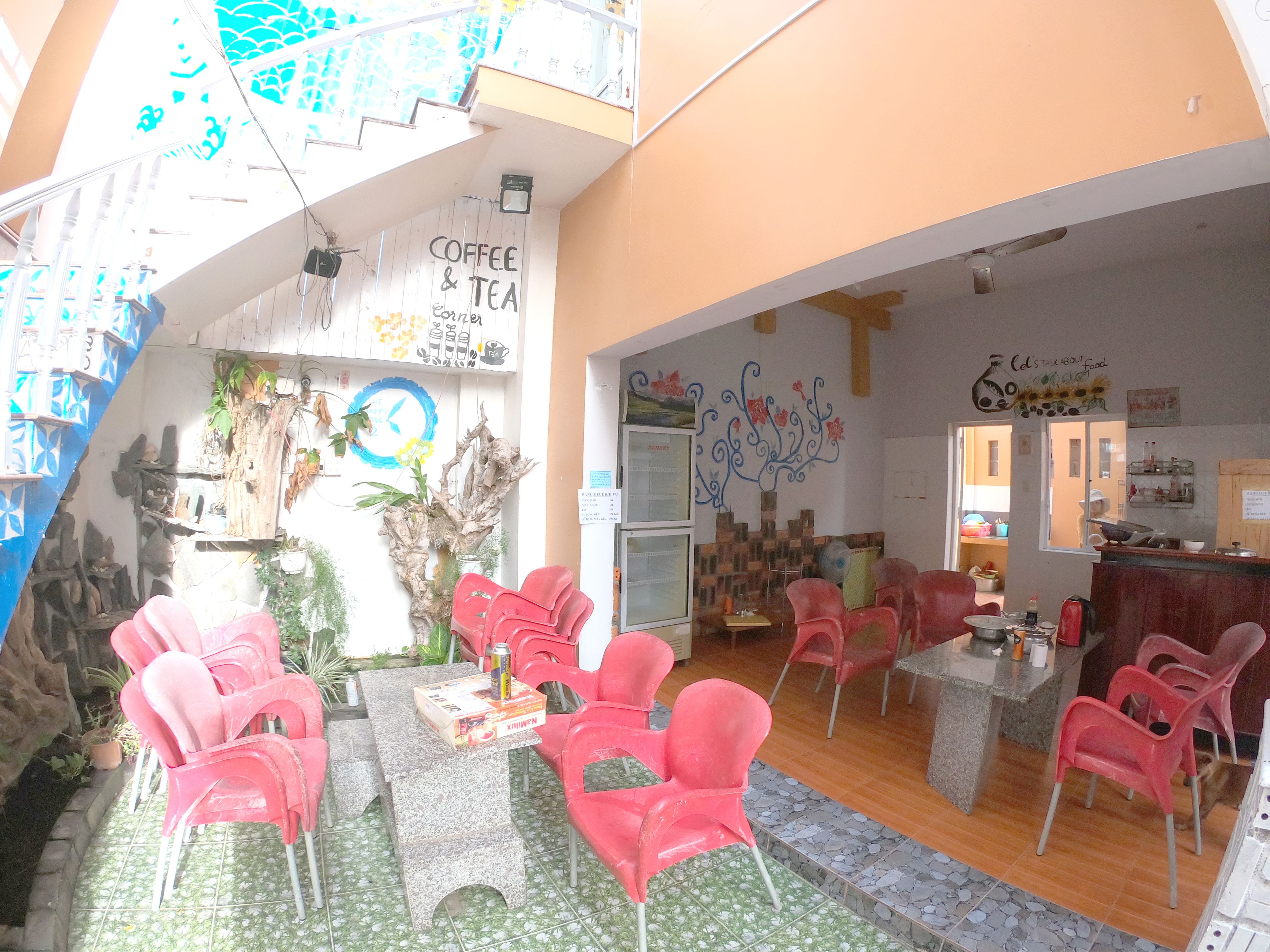 A cozy cafe with a rustic interior, featuring a coffee and tea sign, red chairs, a tiled floor, and a wooden ceiling.