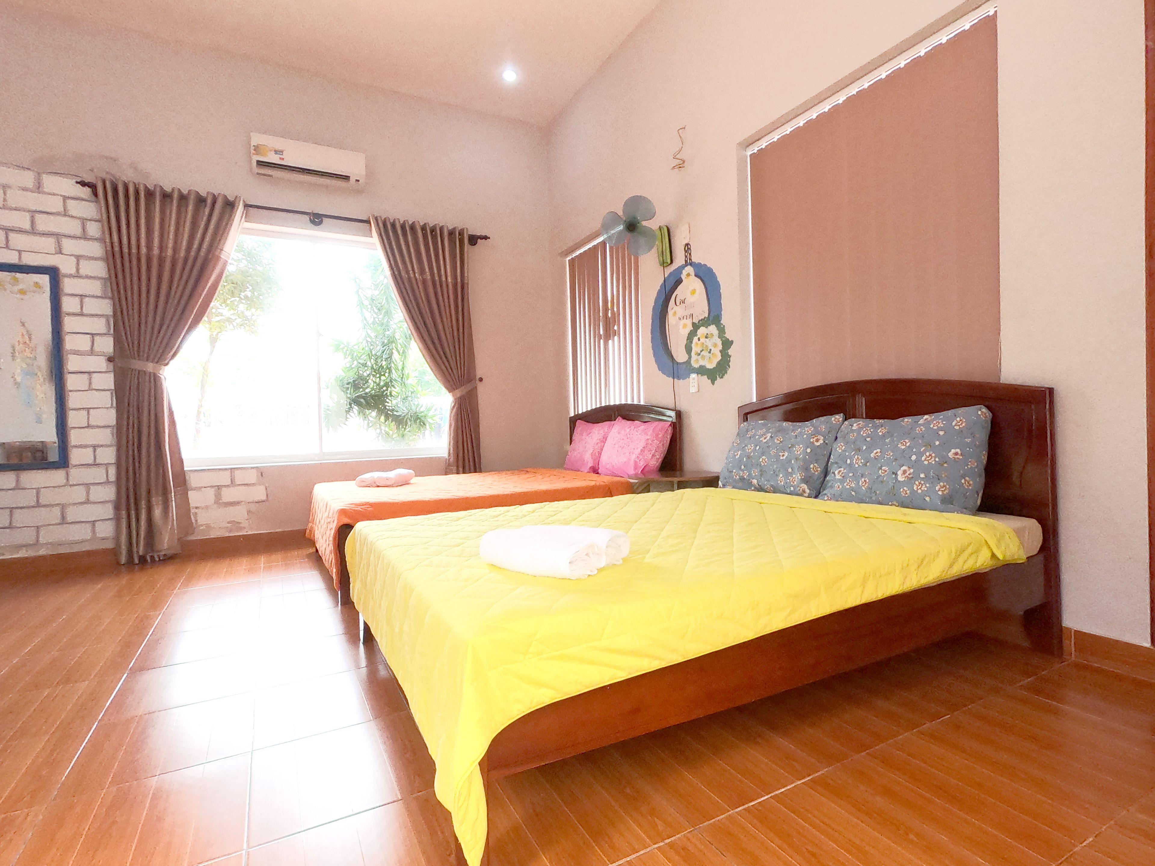 Une chambre d’hôtel avec deux lits, un mur en briques, une fenêtre avec des rideaux et un appareil de climatisation.
