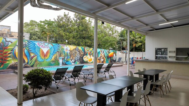 An indoor dining area with tables and chairs, a mural with wildlife and flowers, and a view of trees outside. - Allegro Hotel (Goiania)