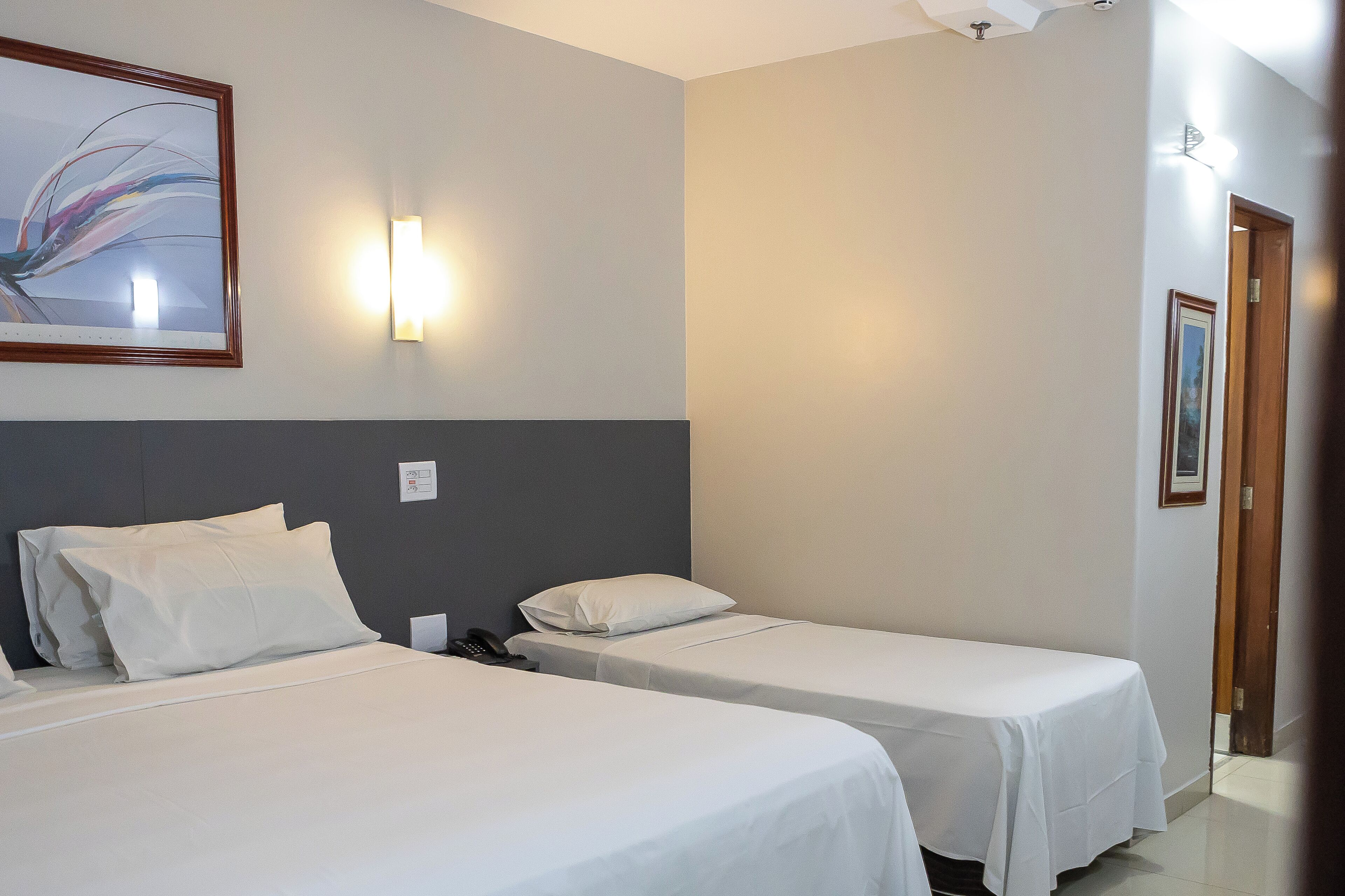 Habitación de hotel con dos camas individuales, una mesita de noche con teléfono, una lámpara de pared y un cuadro.