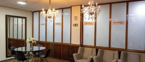 A hotel lobby with a round table, chairs, a chandelier, and a reception area with chairs and a sign.