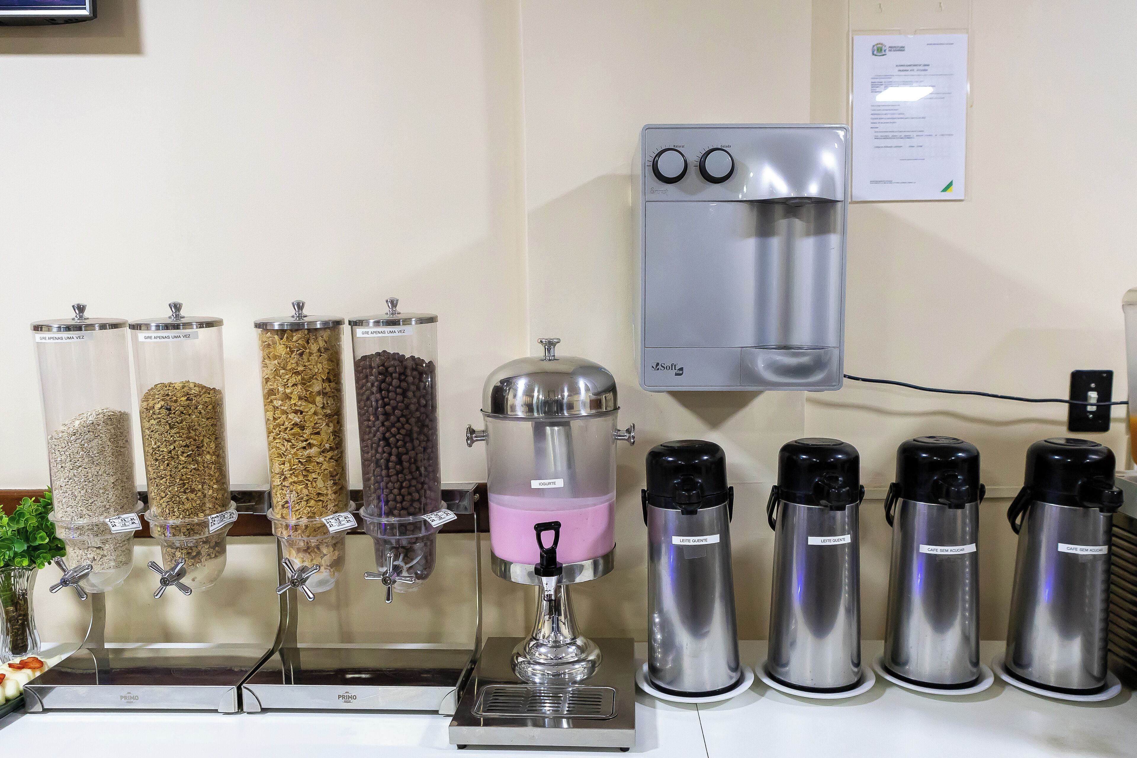Un espacio para bebidas con dispensadores y vasos térmicos, una máquina de café y un dispensador de agua.