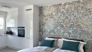 A modern bedroom with a bed, two pillows, a nightstand, and a large window. - Bijou Lido Golf (Ascona)