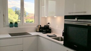 A modern kitchen with white cabinets, a black oven, and a window with a view of mountains. - Bijou Lido Golf (Ascona)