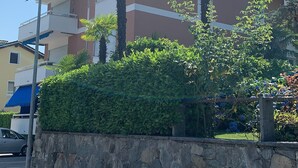 A multi-story building with a stone wall in the foreground, a clear blue sky, and a parked car. - Bijou Lido Golf (Ascona)