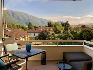 A balcony with a table, chairs, and a view of a mountainous landscape. - Bijou Lido Golf (Ascona)