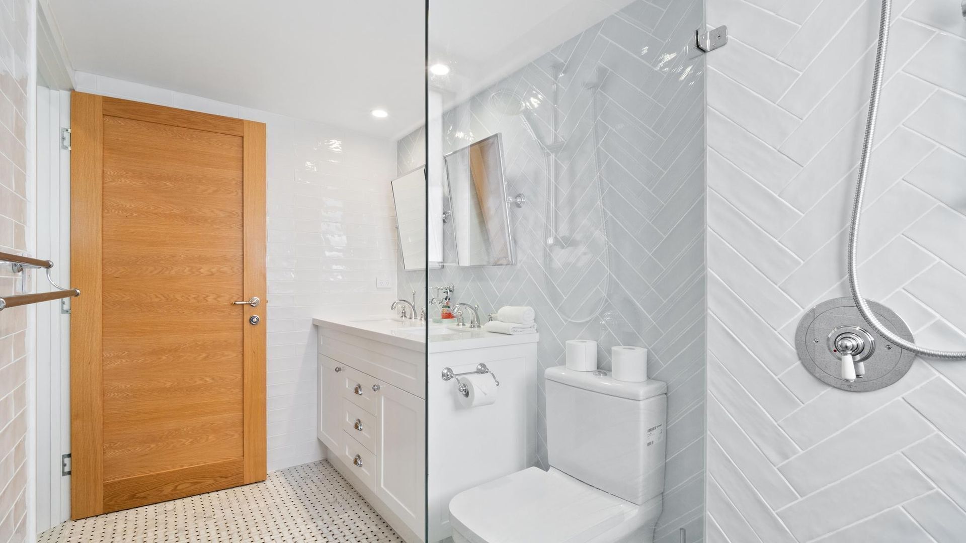 Un bagno moderno con una porta in legno, un box doccia in vetro e un pavimento piastrellato di bianco.