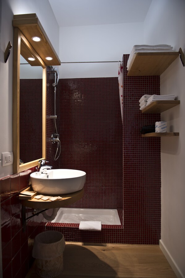 Un baño con lavamanos blanco, espejo, ducha y paredes con azulejos rojos.
