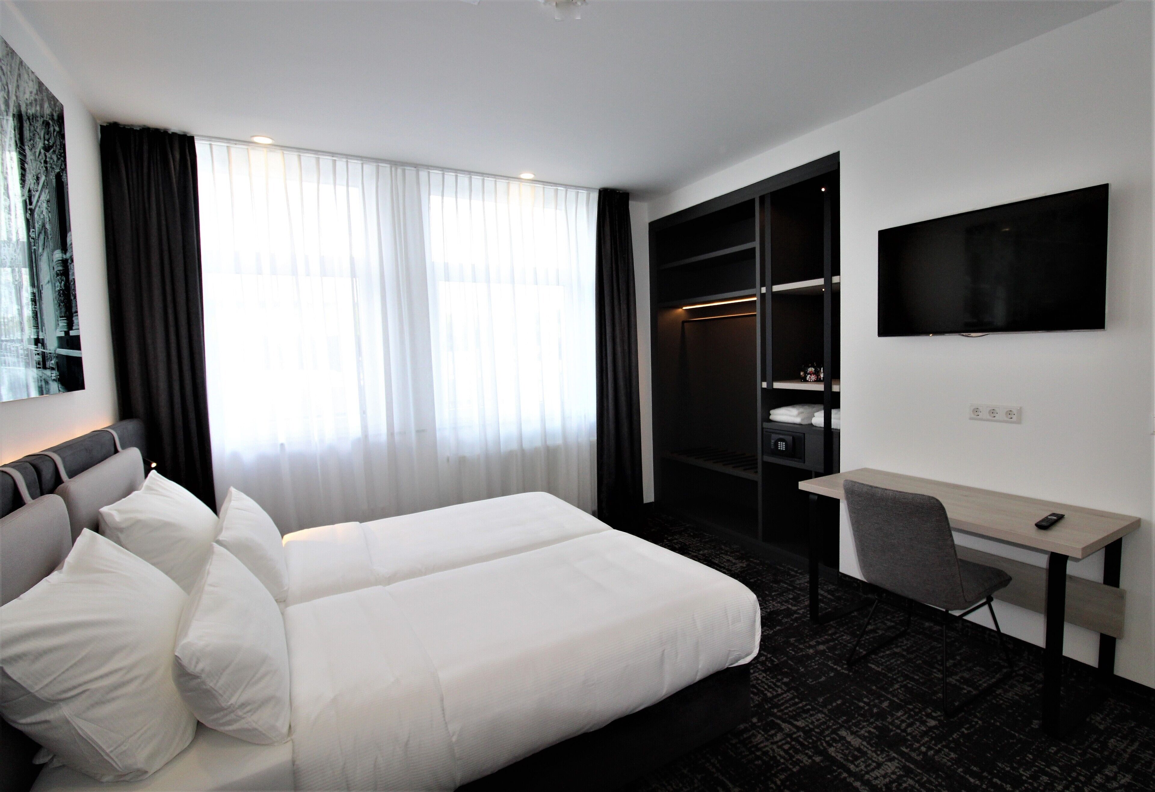 A hotel room with a bed, a desk, a chair, a TV, and a wardrobe.