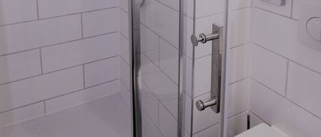 Een moderne badkamer met een douchecabine van glas, witte betegelde wanden, een toilet en een klein aanrecht met een spiegel.