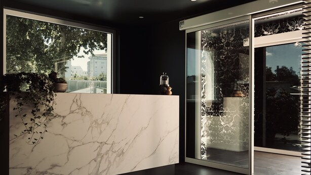 A modern reception area with a marble counter, large windows, and a glass door leading to a balcony.