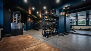 A gym with exercise equipment, a wooden bench, and a view through large windows.