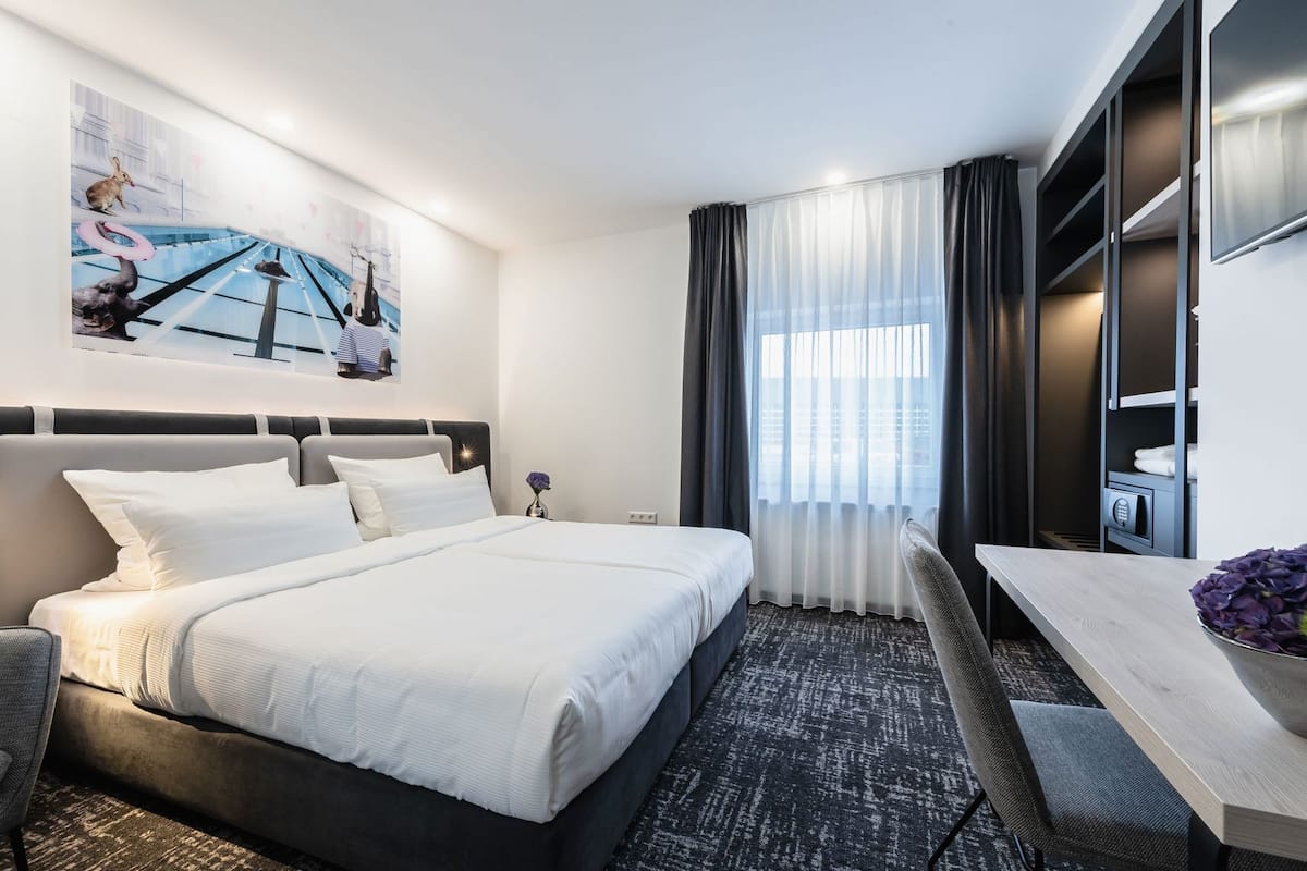 Moderni hotellihuone, jossa on suuri sänky, työpöytä, tuoli, televisio ja vaatekaappi.