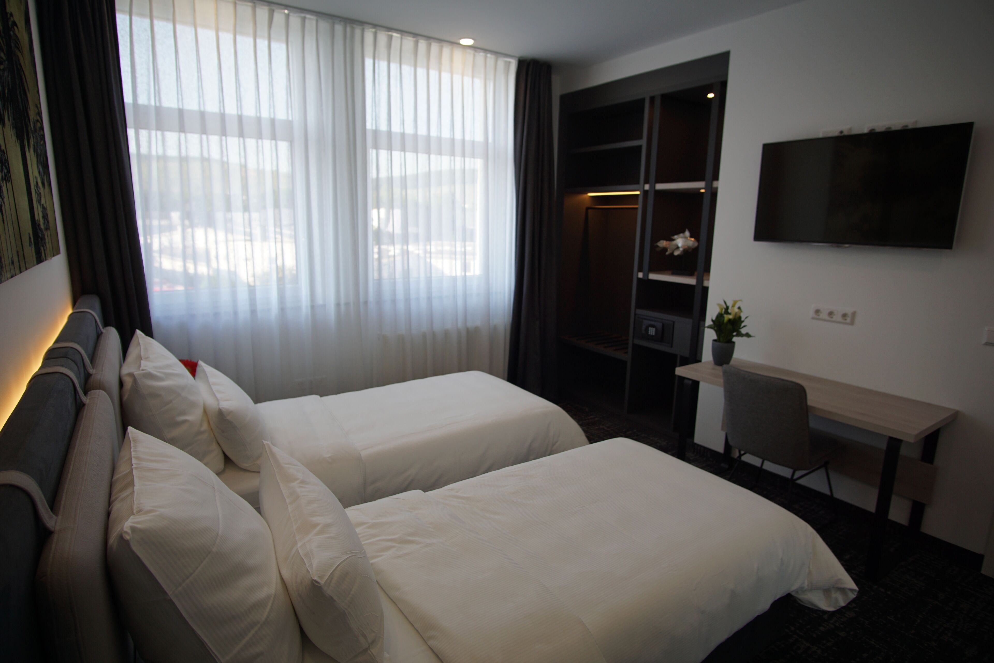 Une chambre d’hôtel avec deux lits, un bureau, une télévision et une grande fenêtre avec des rideaux.