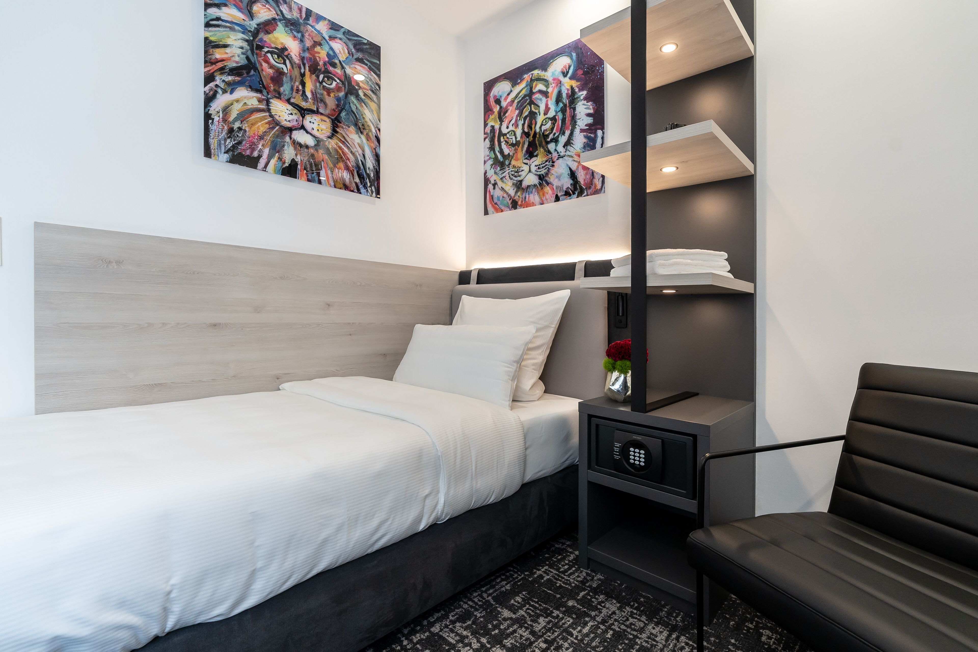 A modern hotel room with a bed, a nightstand, a chair, and two abstract paintings on the wall.