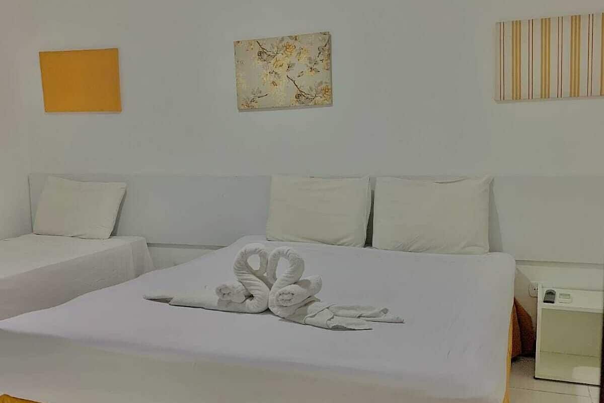 Quarto de hotel com uma cama grande, duas camas menores, uma mesa de cabeceira e uma obra de arte na parede.