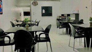 A modern dining area with multiple tables and chairs, a ceiling fan, and a microwave.