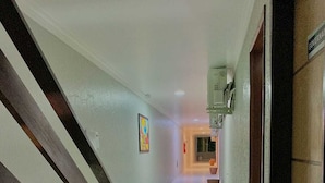 A hallway with a staircase on the left, a potted plant, and a sign on the right.
