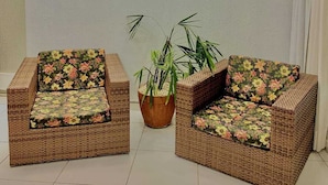 A room with two wicker armchairs with floral upholstery, a potted plant, and a plain wall.
