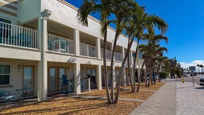 A multi-story hotel with balconies, palm trees, and a pebble-lined walkway.