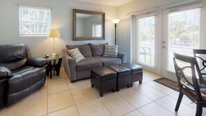 A living room with a grey sofa, a black leather chair, a small table with a lamp, and a large mirror on the wall.