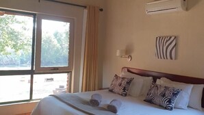 Et hotelværelse med en stor seng, et vindue med gardiner, en aircondition samt en vægdekoration med zebramønster.