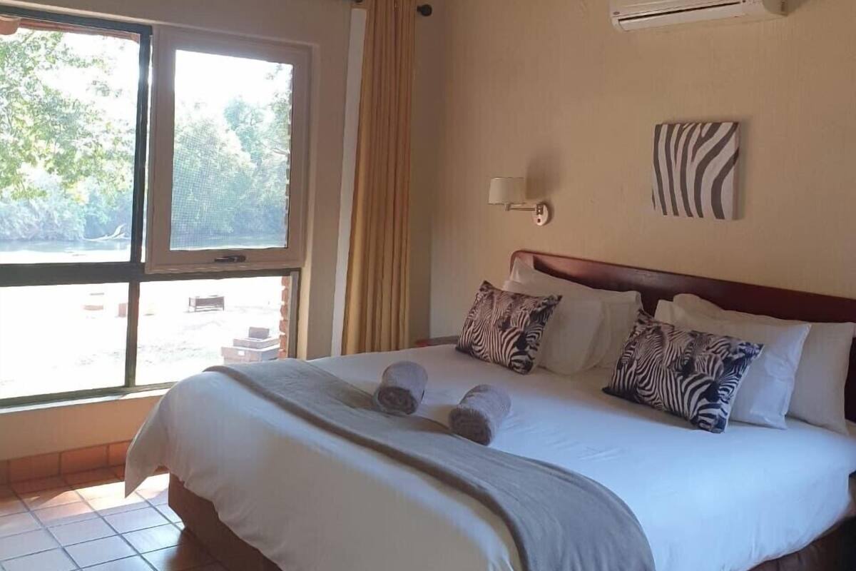 Une chambre d’hôtel avec un grand lit, une fenêtre avec des rideaux, un appareil de climatisation et un motif zébré sur un des murs.