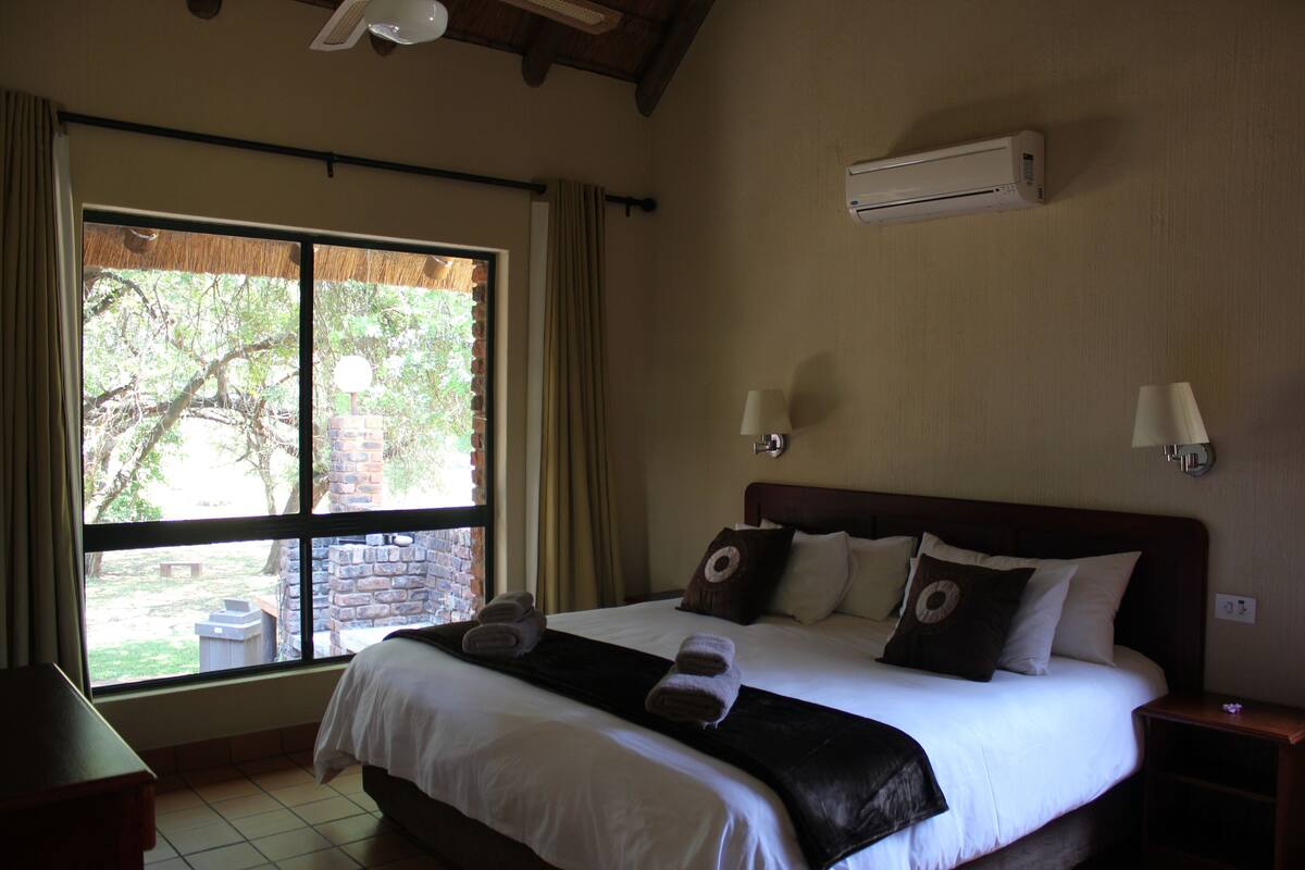 Une chambre d’hôtel dotée d’une grande fenêtre, d’un lit avec du linge de lit blanc, d’une tête de lit sombre et de deux lampes fixées au mur.