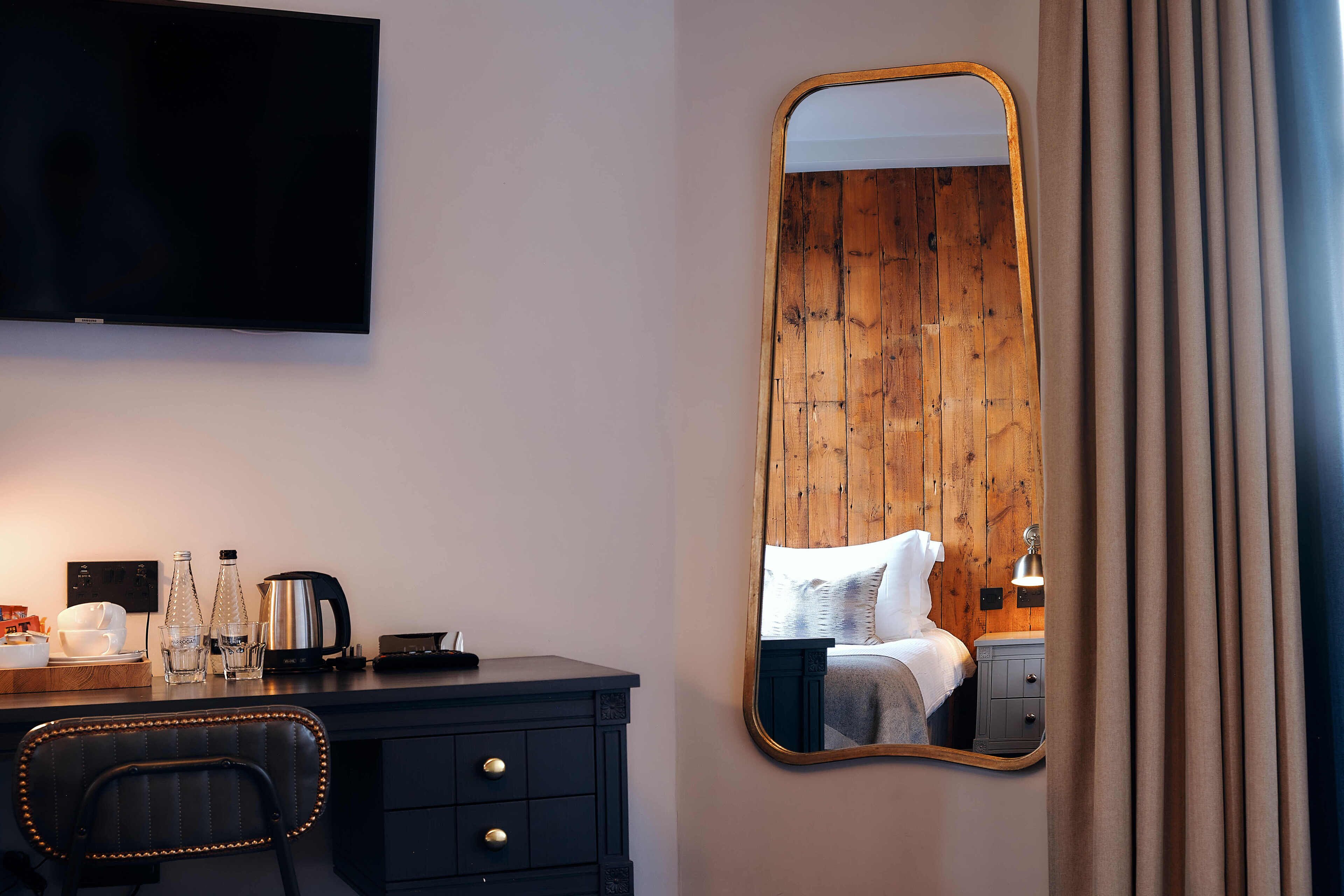 Habitación de hotel con pared de madera, un espejo grande, un televisor de pantalla plana, un escritorio con una silla y una cama con una mesita de noche.