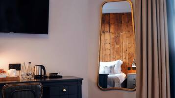 Habitación de hotel con pared de madera, un espejo grande, un televisor de pantalla plana, un escritorio con una silla y una cama con una mesita de noche.