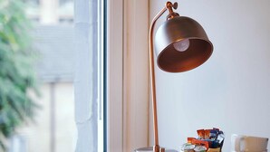 A hotel room with a desk, a chair, a lamp, a tray with cups and a mug, and a framed picture on the wall. - The Brownswood (London)