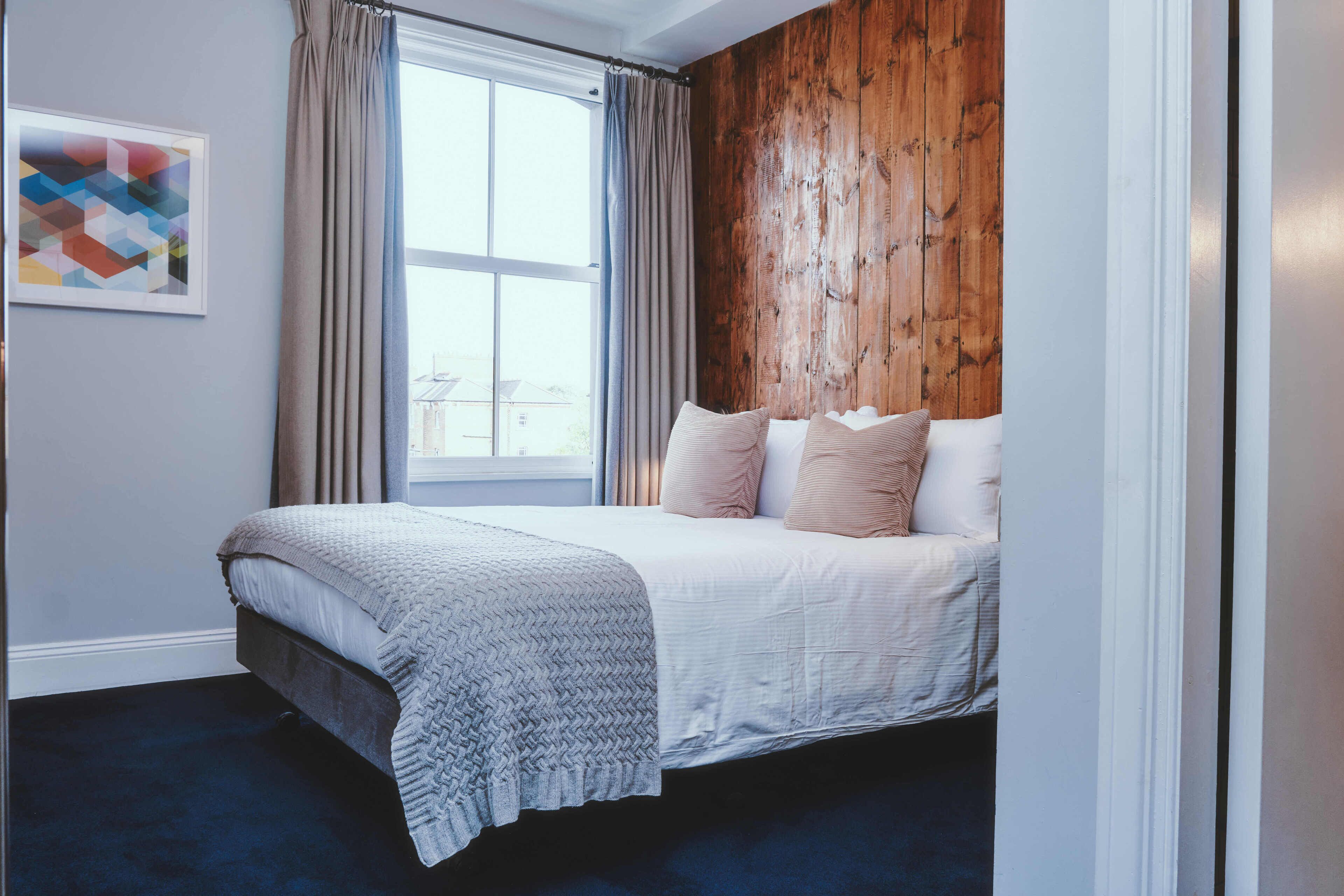 A bedroom with a bed, a window with curtains, a wooden wall, and a framed picture on the wall.