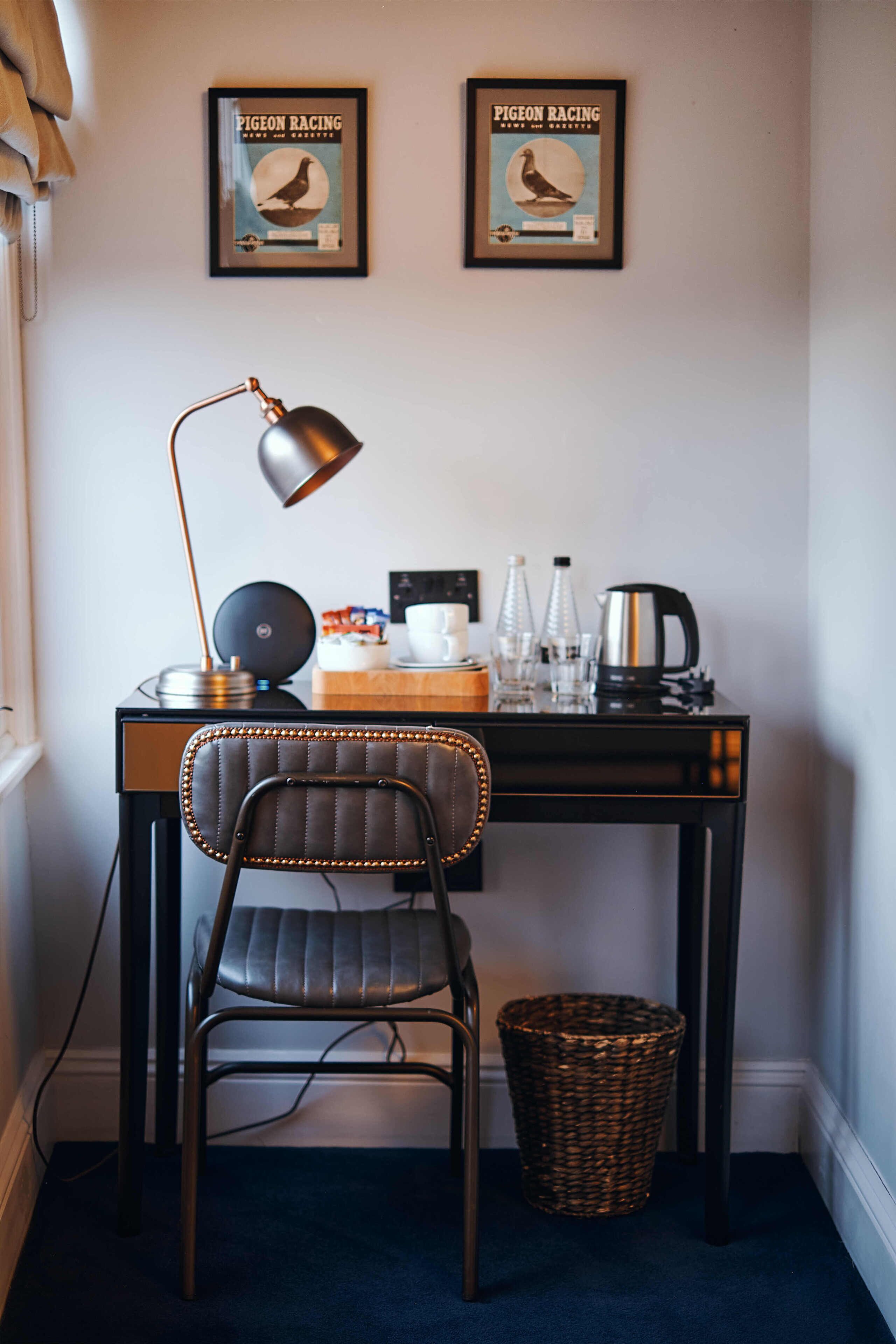 A small office space with a desk, chair, lamp, and two framed pictures on the wall.