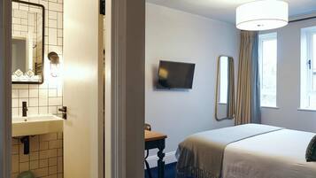 Hotelkamer met een bed, televisie, spiegel, raam met gordijnen en een badkamer met wastafel en spiegel.