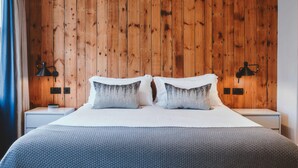 A bedroom with a wooden headboard, two bedside tables, a bed with a white duvet and grey pillows, and two wall-mounted lamps. - The Brownswood (London)