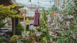 An outdoor patio area with wooden tables and chairs, surrounded by greenery and potted plants. - The Brownswood (London)