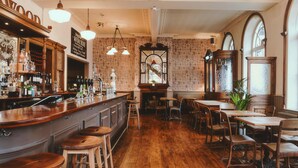 A bar area with stools, a counter with bottles, and a mirror. There are tables and chairs in the dining area. - The Brownswood (London)