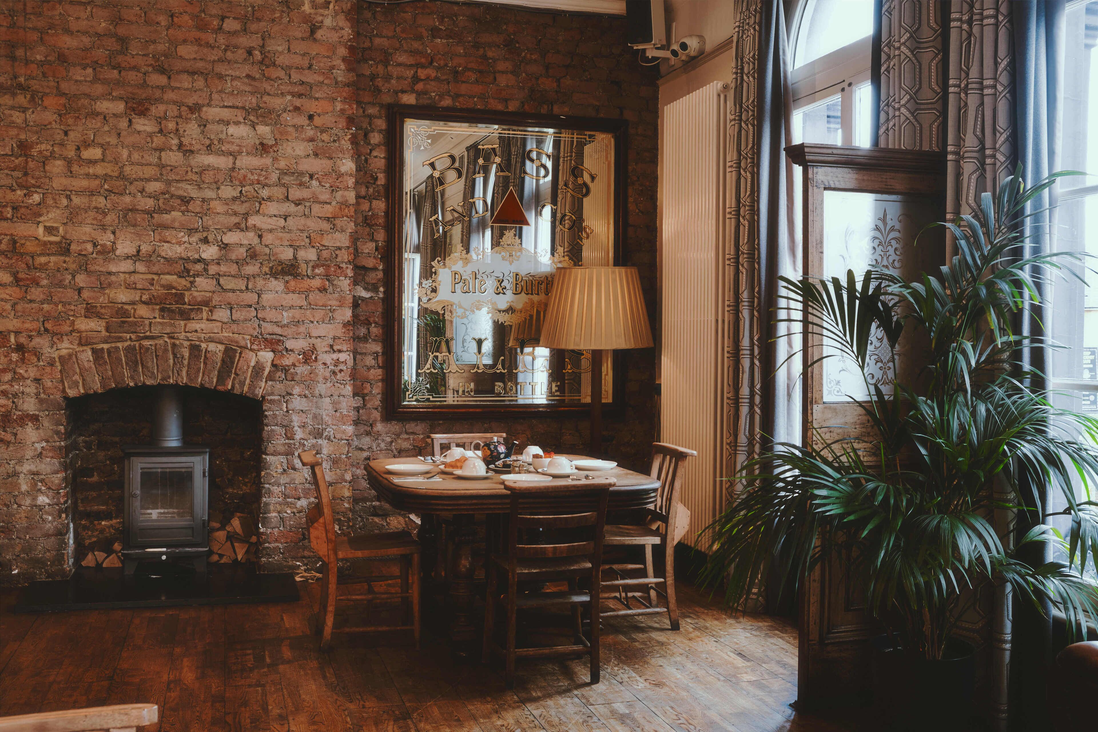 Un interior rústico con chimenea de ladrillo, una mesa de comedor para cuatro personas y un espejo grande que refleja la estancia.